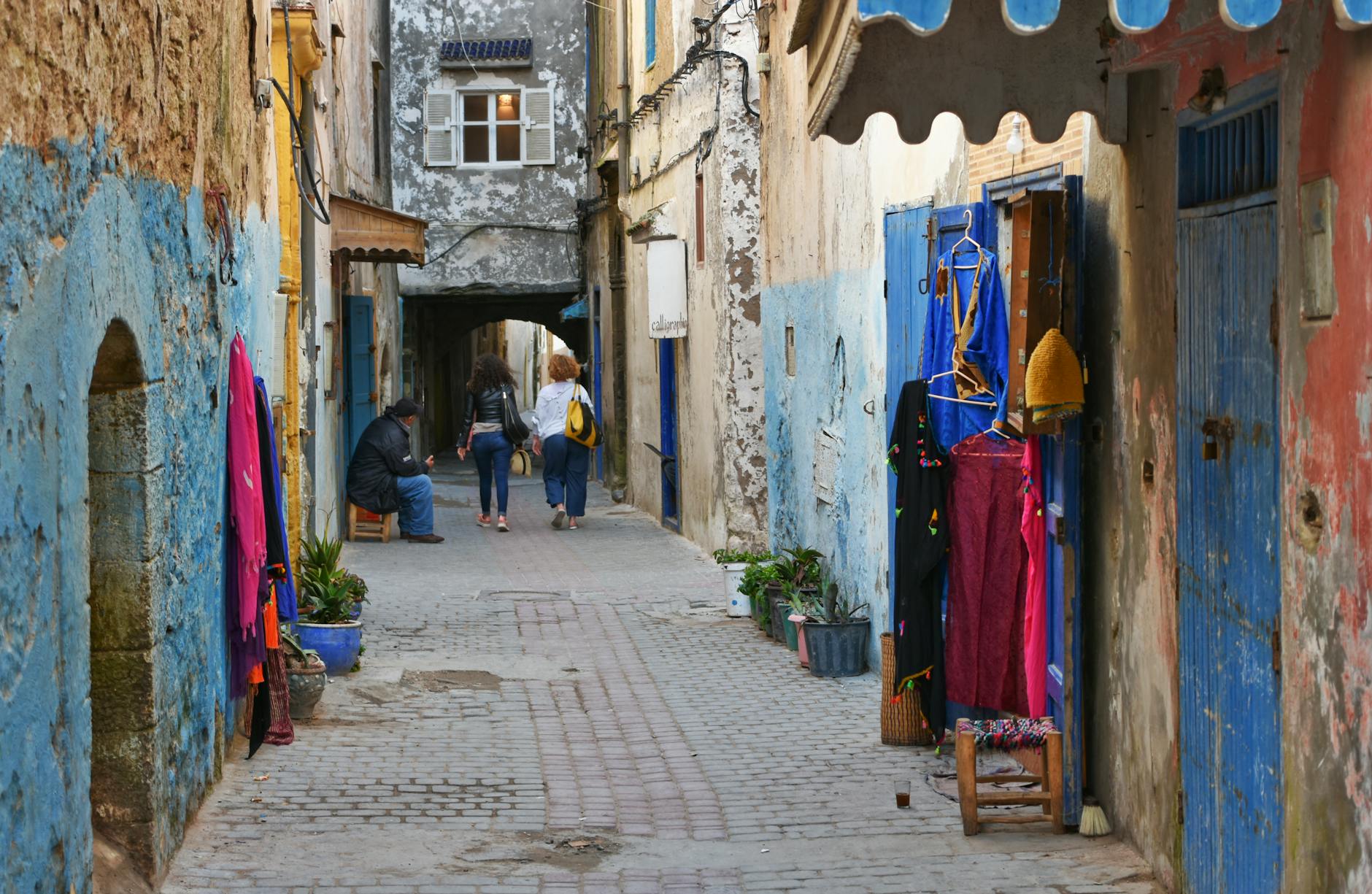 Charming alley in Essaouira with vibrant textiles and historic architecture.