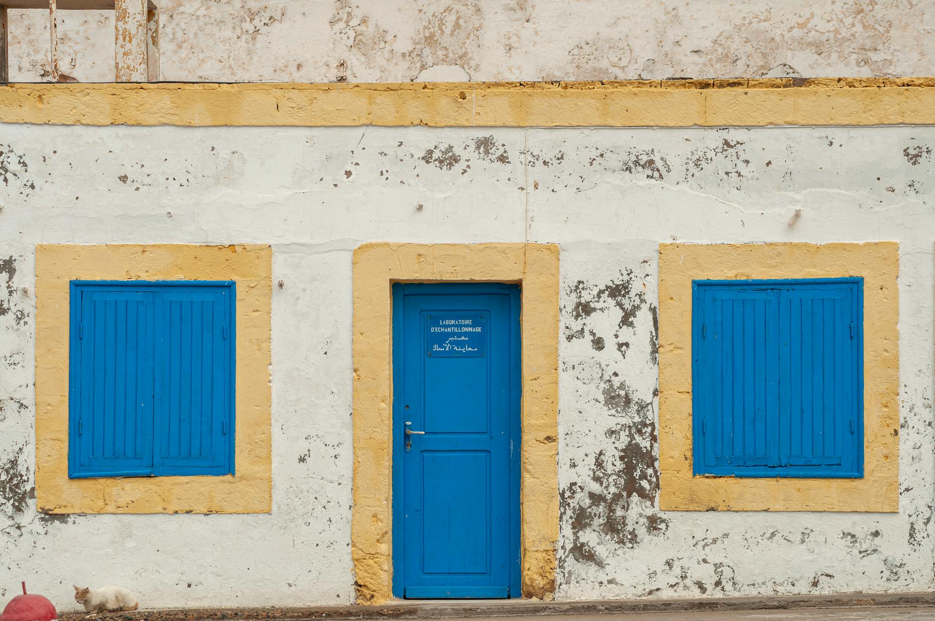 Exterior of aged stone weathered residential house with bright blue wooden door and shuttered windows in old town in Morocco