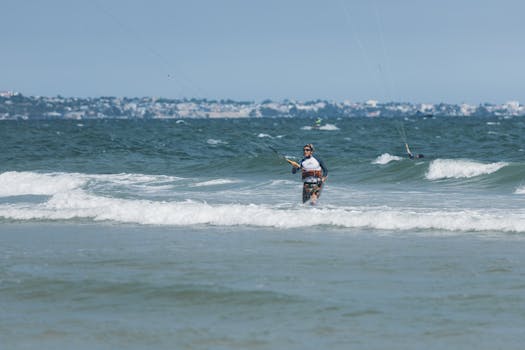 A kitesurfer stands confidently in the waves, ready for adventure on a sunny beach day.