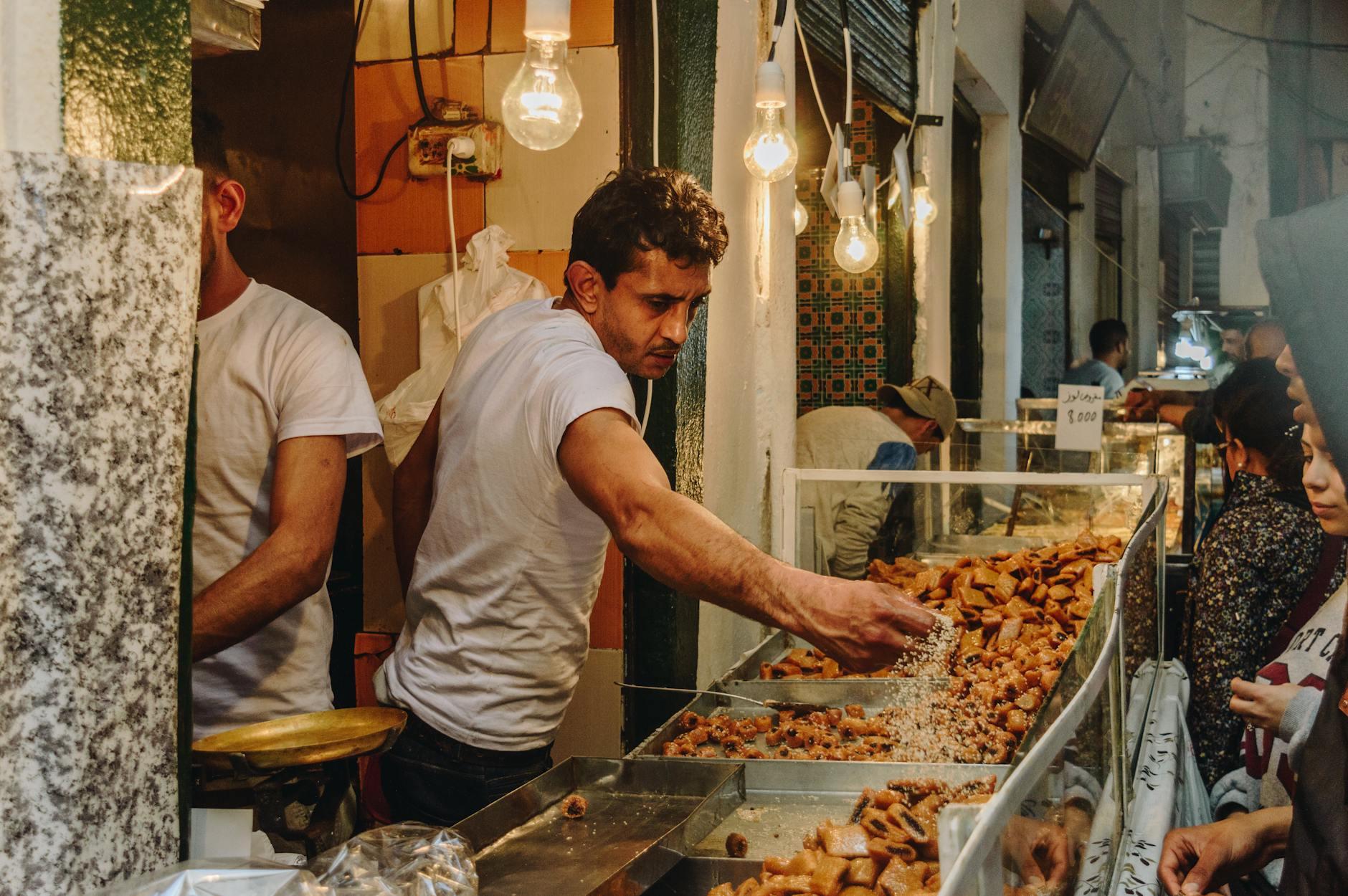 A vendor in a bustling market serves traditional sweets to customers.