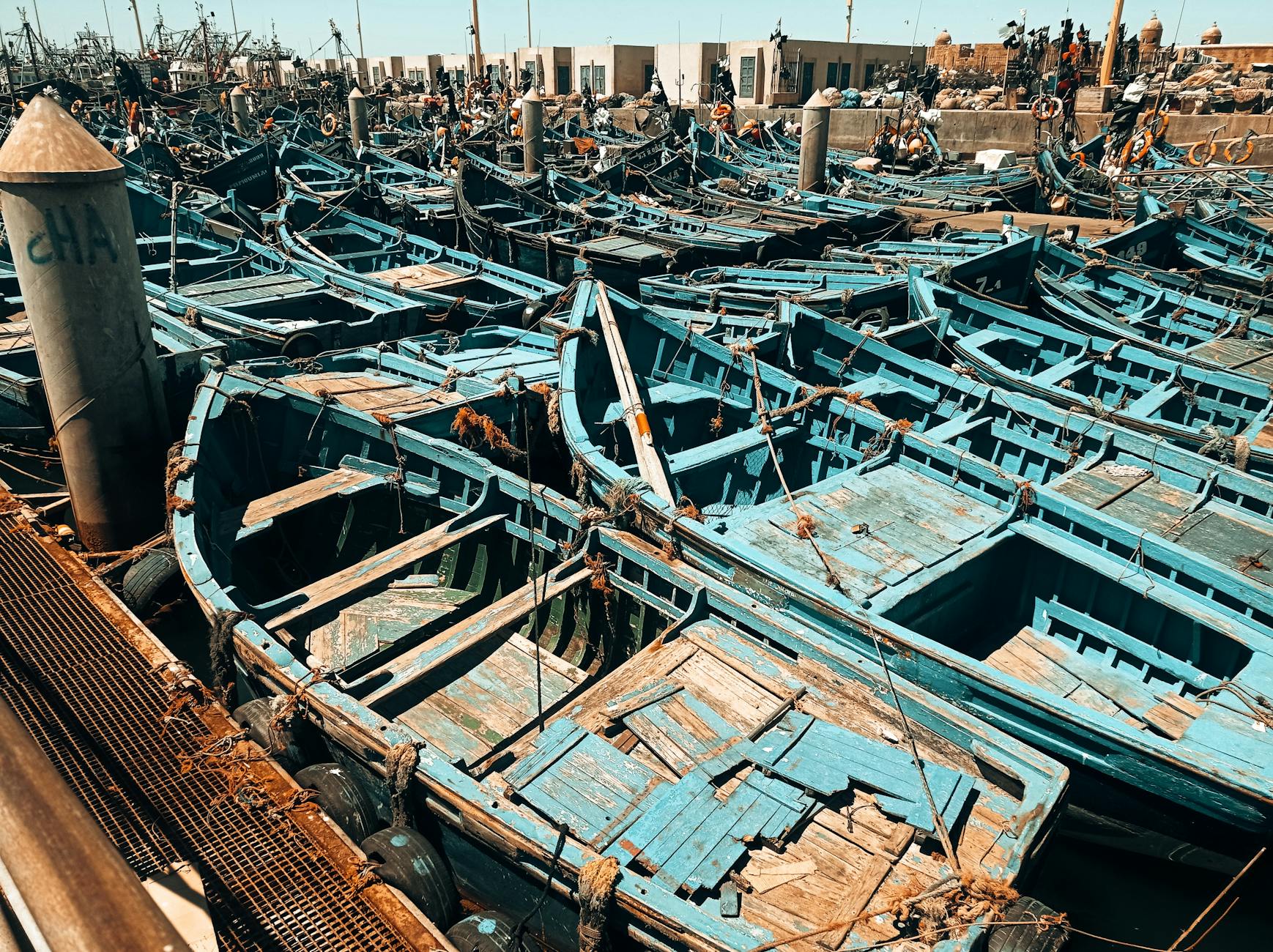 A crowded harbor scene with traditional wooden fishing boats docked at a busy port under a clear sky.