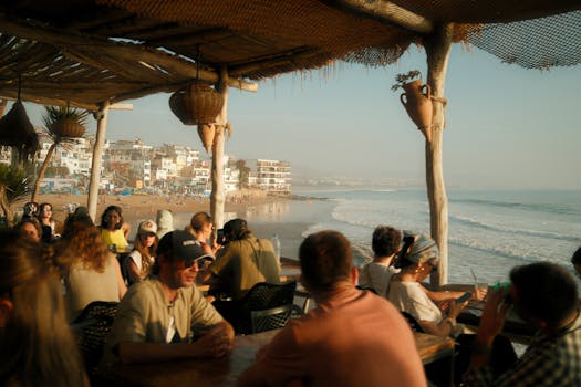 A serene cafe by the Moroccan seaside with people enjoying the sunset view over the ocean.
