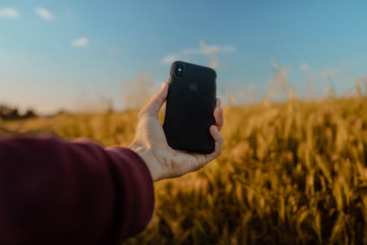 A person's hand holding a smartphone in a scenic wheat field in Morocco.