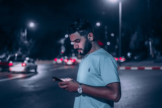 A focused young man checks his smartphone on an illuminated street at night in Rabat, Morocco.
