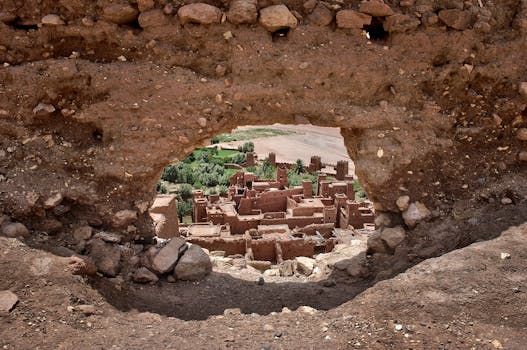 View of a historic village through a natural rocky archway in a desert landscape.